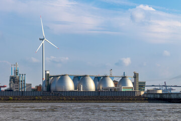 Gas silos in a port facility in front of a wind power plant. Renewable energies vs. gas shortage in...