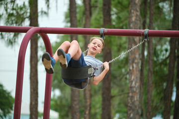Young handsome teenage boy playing alone on playground swings on summer vacations sunny day