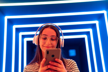 Young meloman using smartphone in neon corridor