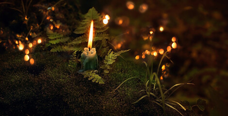 burning candle on moss close up, dark blurred mystery natural background. magic candle for witch...