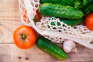 Fresh juicy vegetables, products in a reusable shopping bag, a string bag made of recycled materials, on a wooden table in the garden. Vegetarianism. No plastic. Eco-friendly lifestyle.