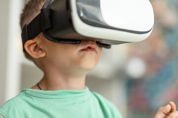 a boy child in a T-shirt wearing a virtual reality helmet imitates behavior in a fictional world, dependence on gadgets and virtual reality. The concept of future technology. selective focus