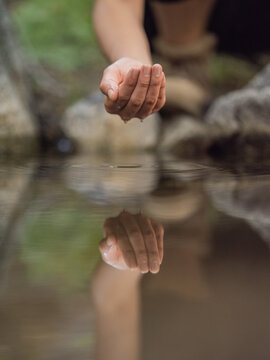Close-up image of a young woman's hands cupping water from a stream 