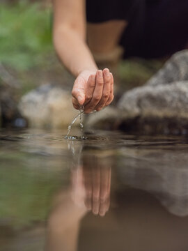 Close-up image of a young woman touching the water from a stream