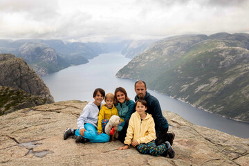 Family, enjoying the hike to Preikestolen, the Pulpit Rock in Lysebotn, Norway on a rainy day, toddler climbing with his pet dog the one of the most scenic fjords