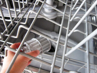  A hand taking out dishwasher filter to clean it, dis washer cleaning concept, kitchen home appliances care and maintenance