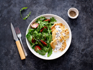 zucchini pancakes with rukolla, tomatoes on white plate on dark background. Top view. Balanced breakfast.