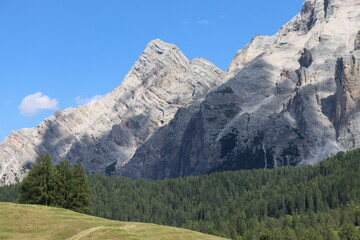 Fototapeta premium Val Badia, Italy-July 17, 2022: The italian Dolomites behind the small village of Corvara in summer days with beaitiful blue sky in the background. Green nature in the middle of the rocks.
