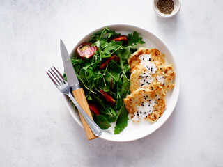 zucchini pancakes with rukolla, tomatoes on white plate on light background. Top view.