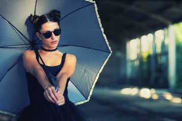 Goth ballerina holding parasol and wearing sunglasses posing in abandoned building