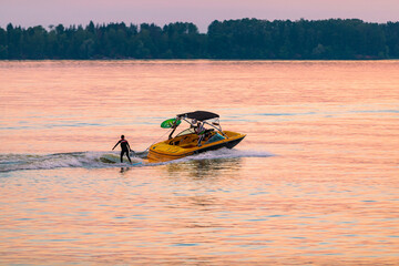 A boat pulls a person over the waves on a wakeboard. Wakeboarding at sunset