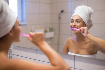 Young woman washing teeth in the bathroom in front of the mirror in morning