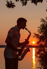 A young guy plays the saxophone in the evening at sunset