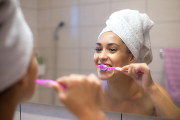 Young woman washing teeth in the bathroom in front of the mirror in morning