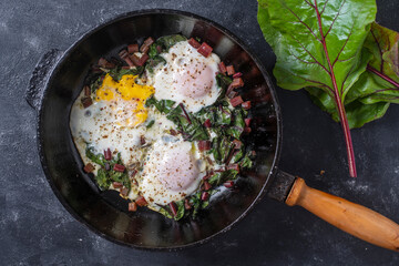 Fried eggs with green beet leaves, onion, pepper and spices in cast iron pan