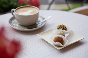 Natural vegan truffles without baking, flour and milk. Cup of cappuccino on wooden table outdoor in the cafe terrace. Coffee break.