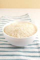 Dry camollino rice in a white ceramic bowl on a striped kitchen towel. Asian food concept. Healthy Eating. Copy space. Selective focus. Vertical orientation.