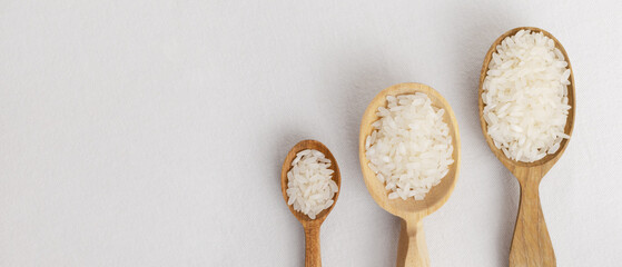 Three wooden spoons of different sizes with Dry camollino rice on a white background. The concept of healthy eating. Horizontal orientation. Top view. Banner