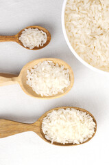 Three wooden spoons of different sizes with Dry camollino rice and bowl on a white background. The concept of healthy eating. Vertical orientation. Top view.