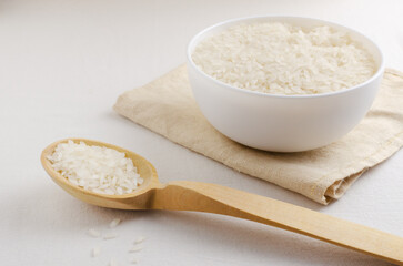 Dry camollino rice in a wooden spoon and a white bowl on a white background. The concept of healthy eating. Horizontal orientation. Rustic style. Copy space.