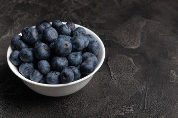 Blueberries in a ceramic bowl on a black textured background. Ripe and fresh blueberries. Vitamins. Healthy food. Juicy berry.Copy space.Place for text