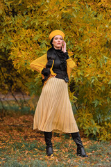 a beautiful brunette with makeup in a yellow beret and yellow jacket walks in the park in autumn.