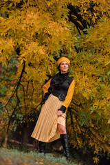 a beautiful brunette with makeup in a yellow beret and yellow jacket walks in the park in autumn.