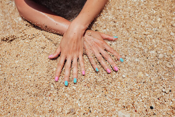 Beautiful female hands with pink and blue manicure nails on sea sand background