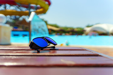 Fototapeta na wymiar Stylish men's sunglasses lie on a sun lounger against the background of the pool on a bright day