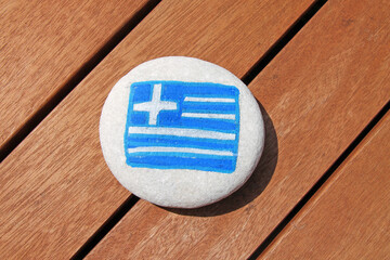 Greece country flag painted on the sea stone on wooden plank background. 