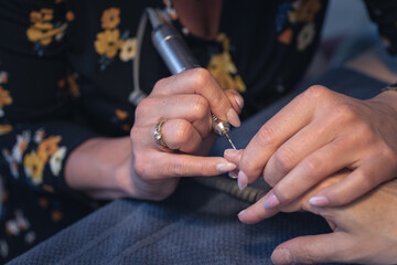 Obraz premium nail grinding and polishing, i.e. professional hardware woman's hand manicure with an electric drill at the client's house. machine removal of protruding cuticles. closeup photo.