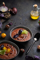 Traditional spanish cold tomato soup gazpacho in a bowl served with basil and cucumber on black textured table with fresh ingredients around. Top view with copy space. Dark mood healthy vegan dish.
