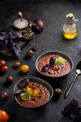 Traditional spanish cold tomato soup gazpacho in a bowl served with basil and cucumber on black textured table with fresh ingredients around. Top view with copy space. Dark mood healthy vegan dish.