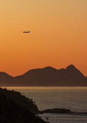 Airplane flying over the mountains at sunrise. Silhouettes and various shades of yellow and orange....