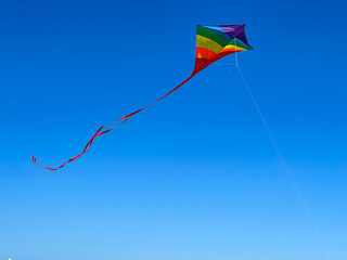 Rainbow Colored Kite Flies High Against Blue Sky Background