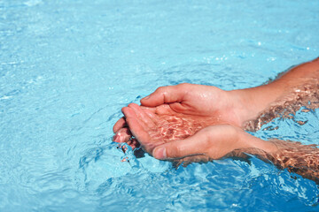 The hands cupped together submerged in clean clear blue water in swimming pool