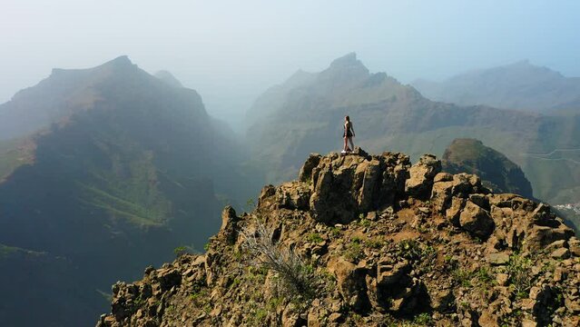 Young hiking girl stands on top of the cliff. Time to trip. Go everywhere. Strength of women. Girls power. Aerial shooting from drone of a woman tourist is enjoying scenery of green mountains.