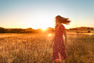 Young woman walking in a field looking to the sunlight with wind blowing her hair. Beauty, freedom...