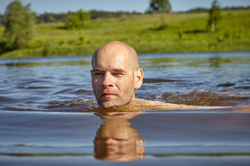 Bald guy swims on the river in summer