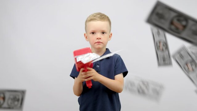 Preschooler boy in blue t-shirt plays with red money gun in white studio