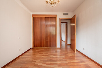 Empty bedroom with built-in wardrobe with sliding wooden doors, French oak parquet floors and matching carpentry.
