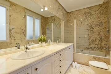 Bathroom with long marble top with two sinks, large frameless mirror on the wall and marble tiling on walls and floors