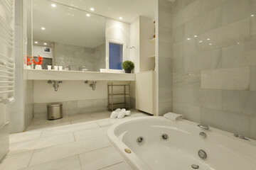 Bathroom with glass mirror covering one wall, long white marble top with two sinks and hydromassage bathtub on the floor