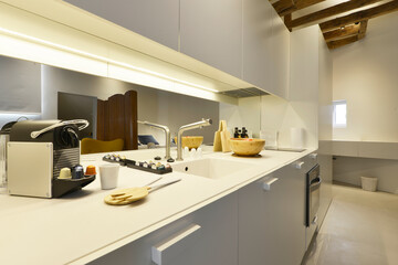 Kitchen with white wooden cabinets, mirrors on the wall, coffee capsule machine, wooden bowl,...
