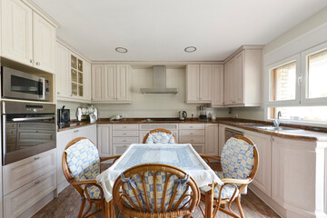 Front view of a kitchen with pale pink white wood cabinets on all walls, built-in appliances, pink granite countertops, and a wooden table and bamboo chairs.