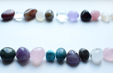 Frame made of semi-precious stones of different colors. Amethyst, rose quartz, agate, apatite, aventurine, olivine, turquoise, aquamarine, rock crystal lie in two rows on a white background.