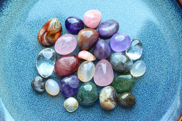 Gemstones of different colors. Amethyst, rose quartz, agate, apatite, aventurine, olivine, turquoise, aquamarine, rock crystal on a blue ceramic plate.