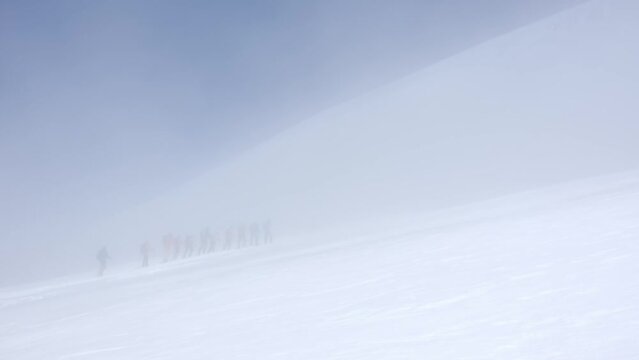 group of skiers is going on snowed mountain slope in snow storm, sportive alpinism and tourism