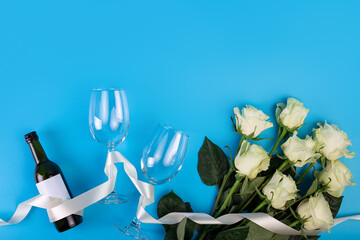 Top view photo of romantic evening, dinner decor hearts love wineglasses with confetti wine bottle and white tape with large bouquet of white roses on isolated blue background with copyspace