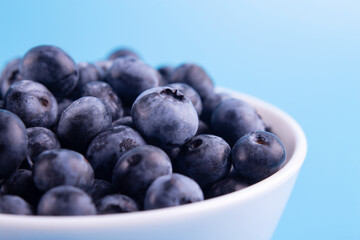 Blueberries on a macro scale. Dark berries in bowl close-up. Ripe blueberries isolated on blue background. Healthy, natural fruit..